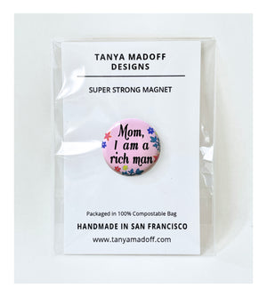 Mom, I Am A Rich Man one inch extra strong magnet, Cher quote featured in Taylor Swift video, with black cursive lettering on pink background with flowers and leaves, packaged on recycled paper, in 100% compostable clear glassine bag